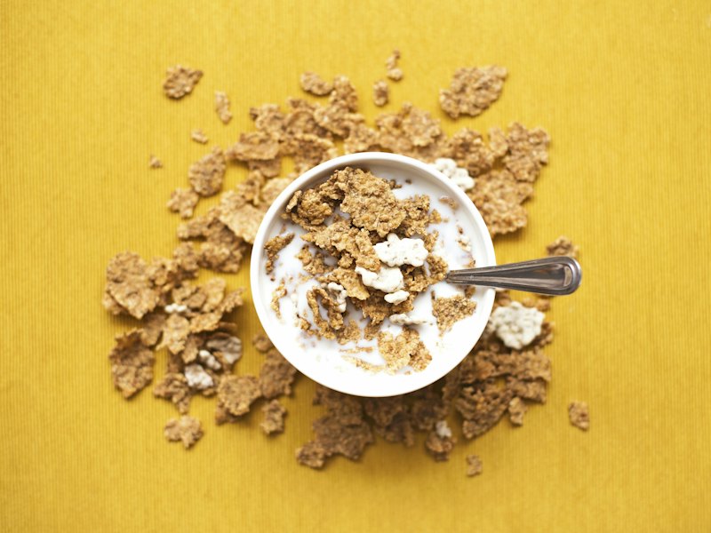 Top view of corn flakes in bowl with milk and silver spoon