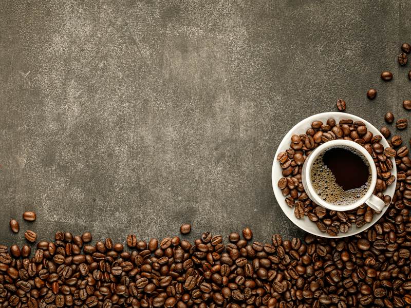 A cup of coffee surrounded by coffee beans